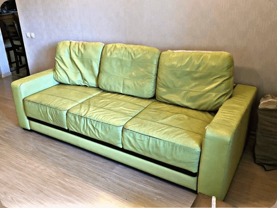 Lime green leather sofa with patchy faded colour and creased panels