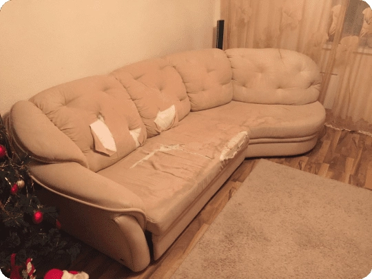 Beige fabric corner sofa torn open along the seat front with filling showing