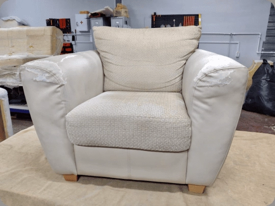Cream leather armchair torn open across both arm tops with foam showing