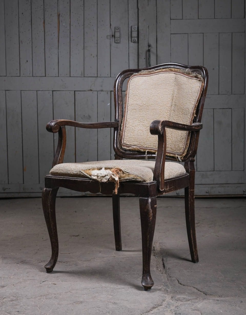 Open-arm cabriole-leg chair before restoration with a shredded cover and stuffing spilling out
