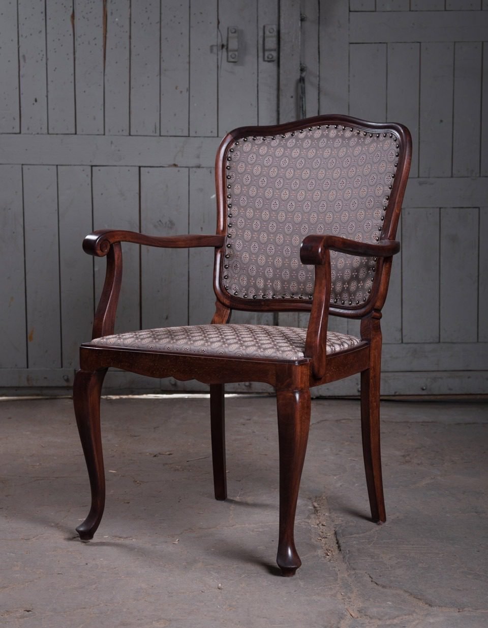 The same open-arm chair after restoration, recovered in grey-mauve printed fabric with close-nailed studs