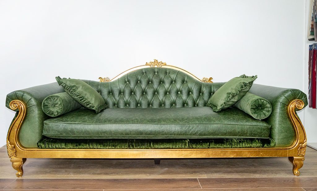 The same giltwood sofa after restoration, recovered in green antiqued leather with a deep-buttoned back