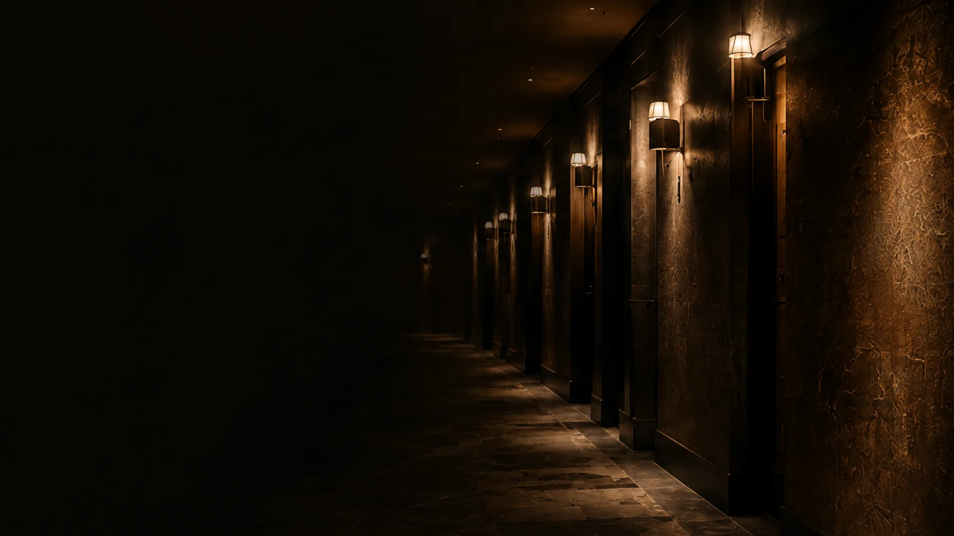 A dark building corridor at night lit by wall sconces
