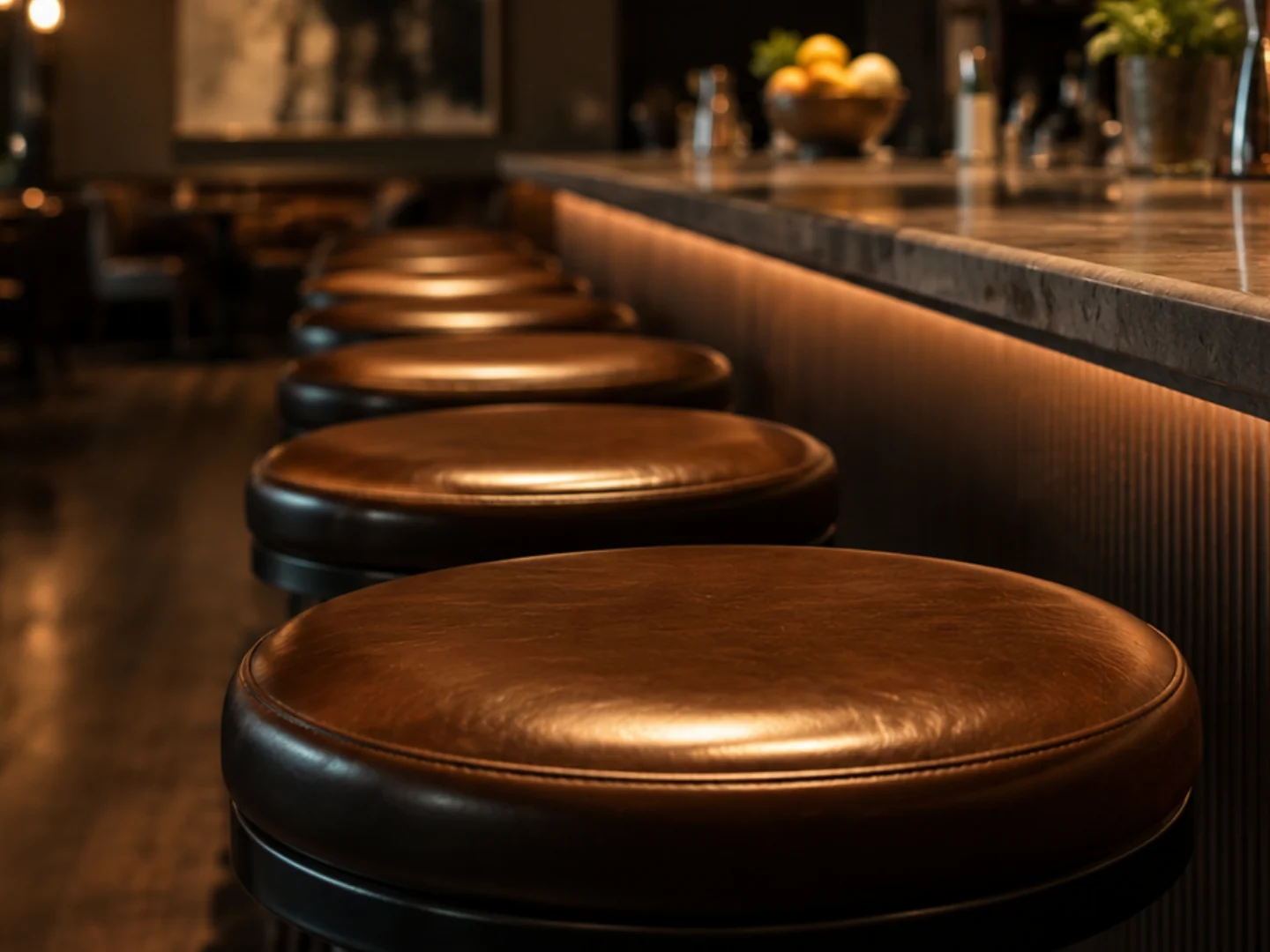 Close view of one cognac leather bar stool seat at the head of a run along a lit bar