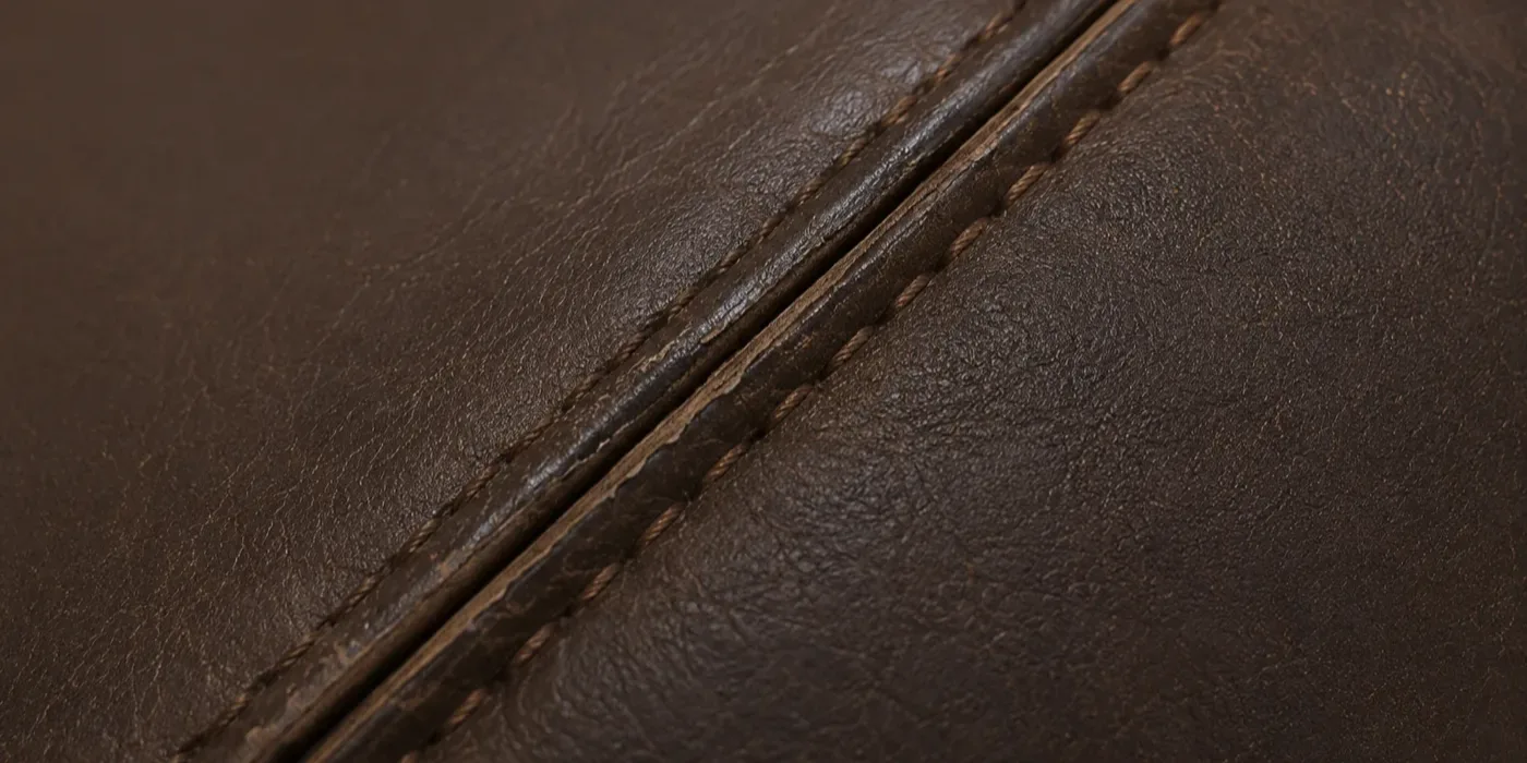 Macro of a rebuilt and re-piped seam on a dark brown leather booth