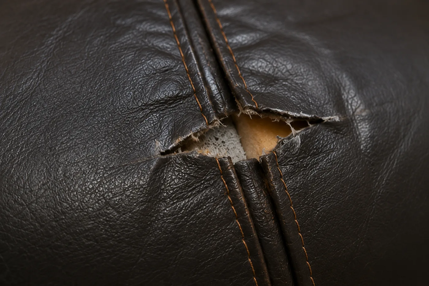 Split seam on a brown leather banquette seat with foam showing through
