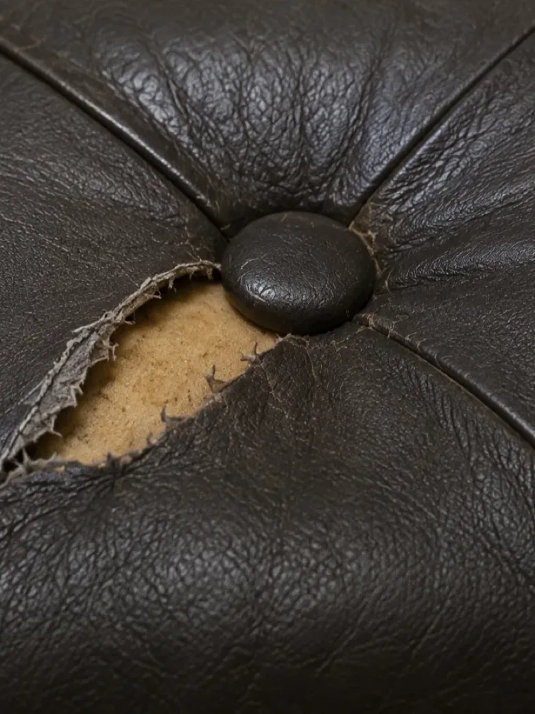 Macro of a tear beside the button of a dark brown buttoned booth, foam showing