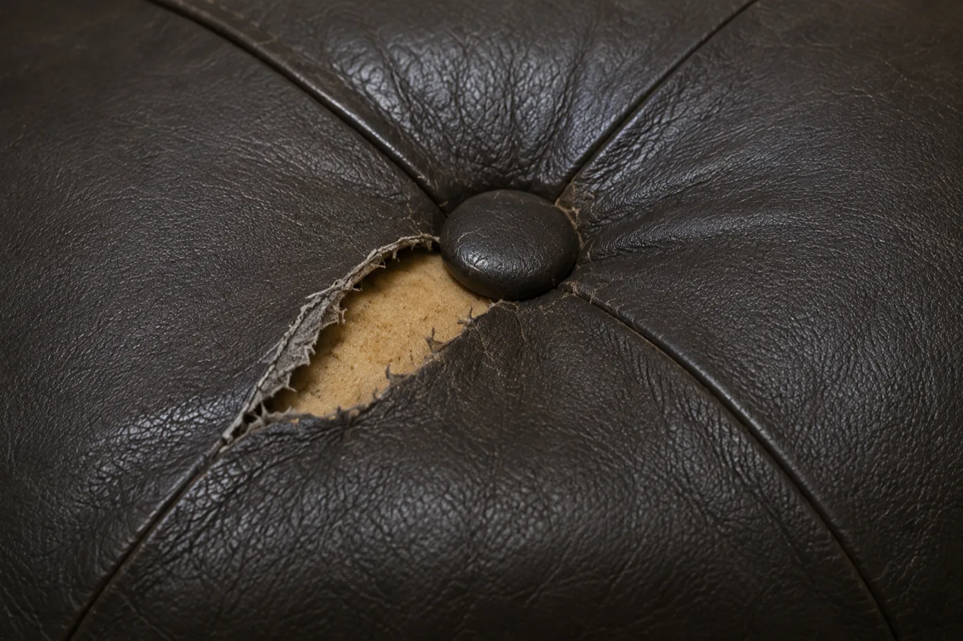 Tear in brown leather beside a deep buttoned banquette back