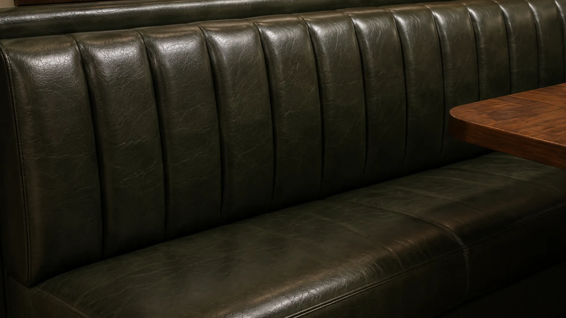 A full bay of a green channeled leather banquette bench built against a wall beside a bar table
