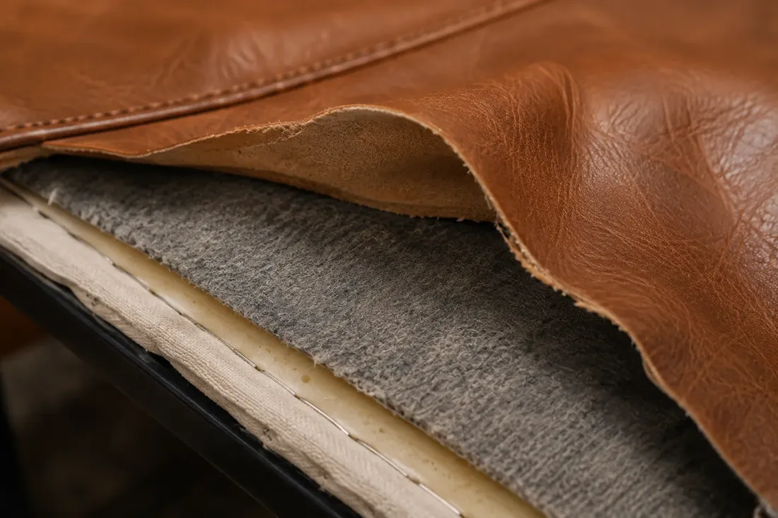 Leather cover peeled back off a cushion, exposing the foam and decking underneath