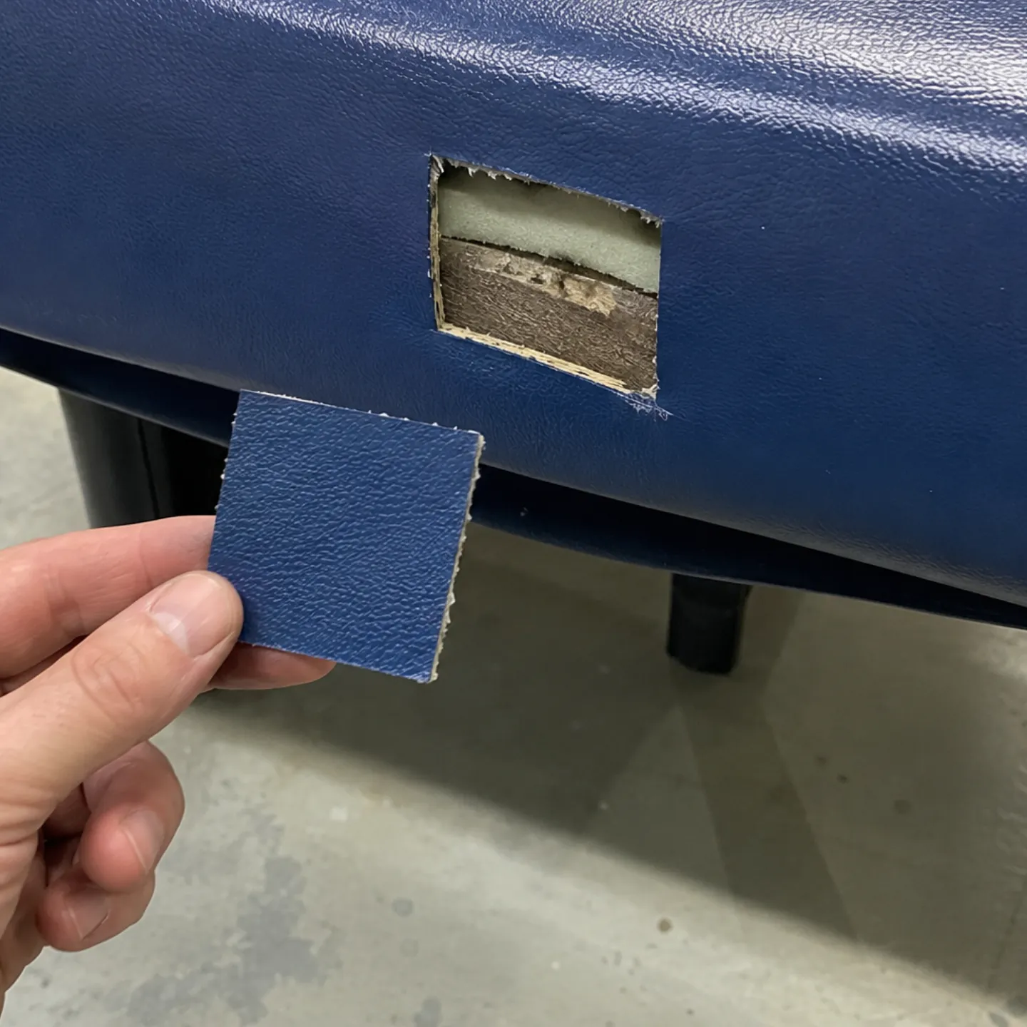 A small blue vinyl sample held beside the hidden spot under a booth seat it was cut from