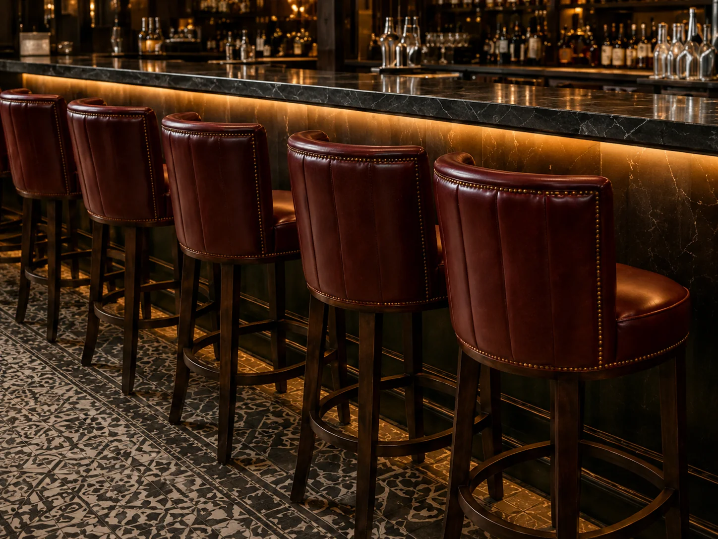 Row of oxblood leather barrel-back bar stools with nailhead trim along a marble bar