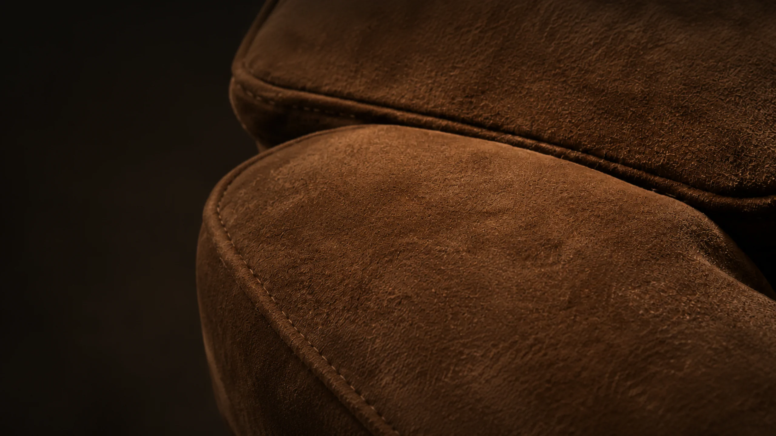 Suede furniture — close view of a brown suede sofa arm and seat cushion, the nap shading lighter and darker across the folds