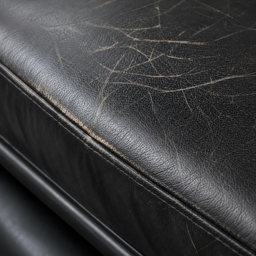 Black leather seat cushion with cracked, faded wear across the surface