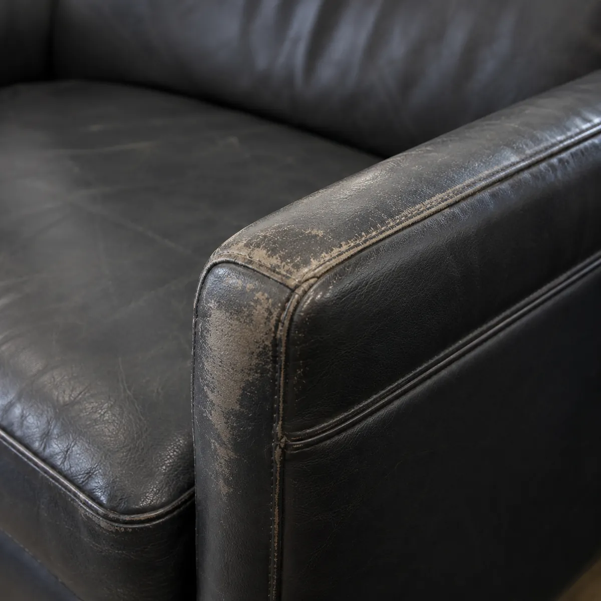 Black leather armrest with the finish abraded down to pale bare hide