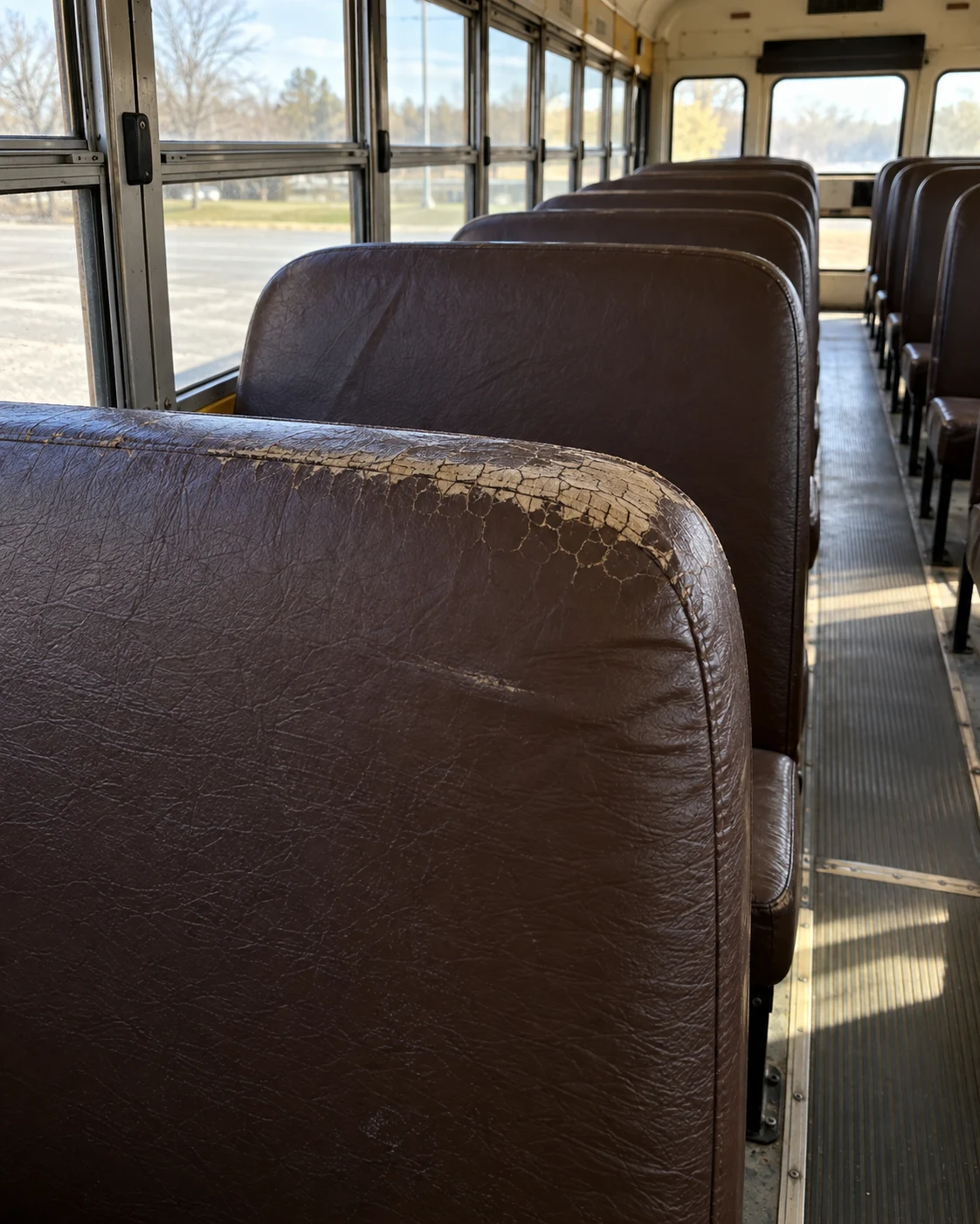 A faded, cracked window-side school bus seat