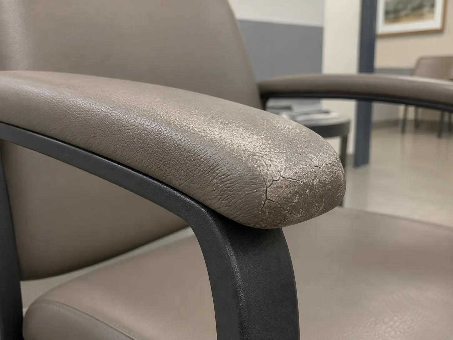 A cracked vinyl arm cap on a waiting room chair before repair