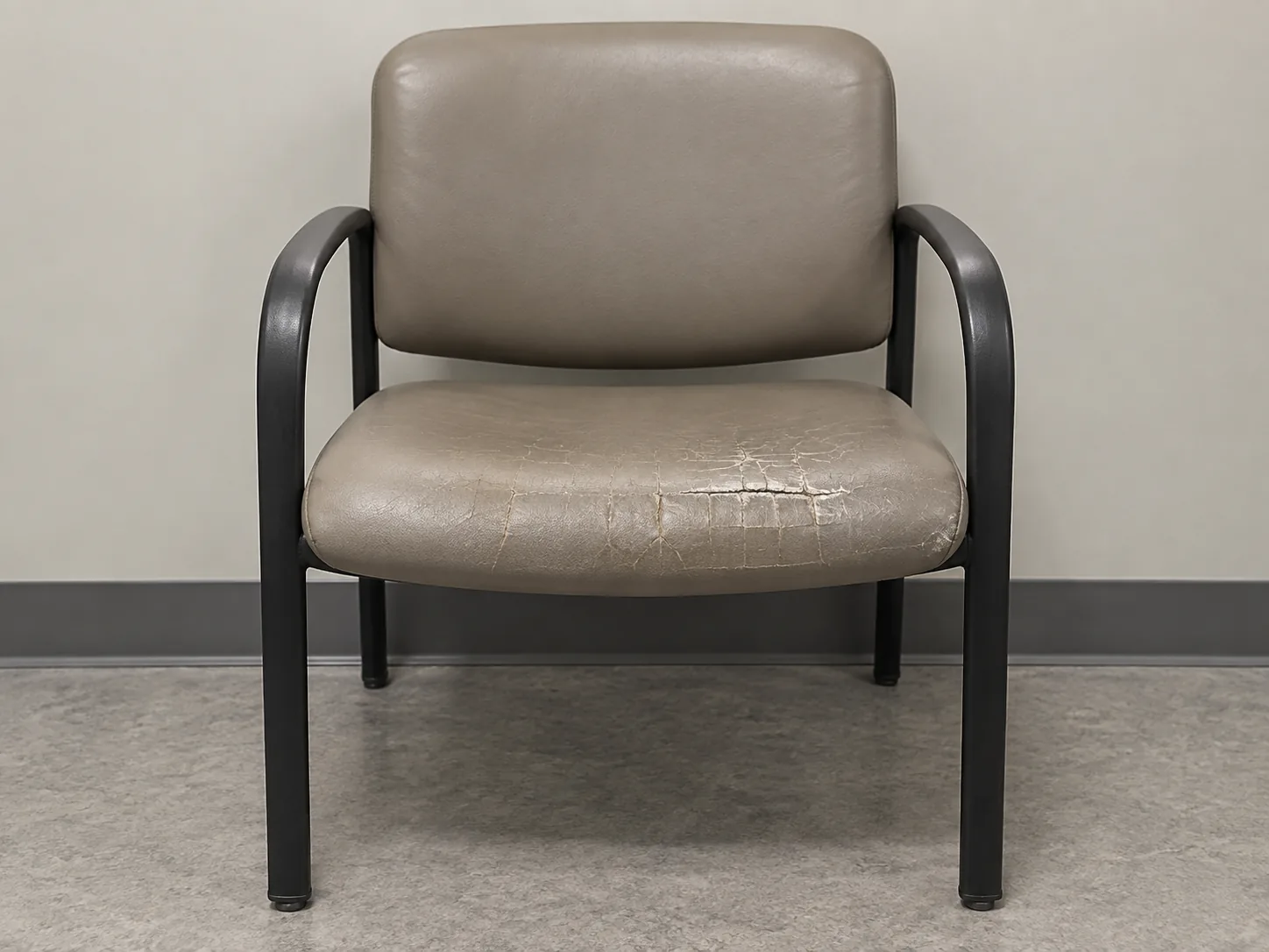 A waiting room chair with a cracked vinyl seat before reupholstery