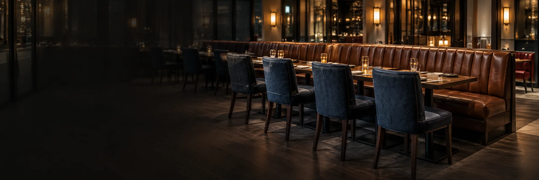 A dim restaurant at night with leather banquettes and blue dining chairs