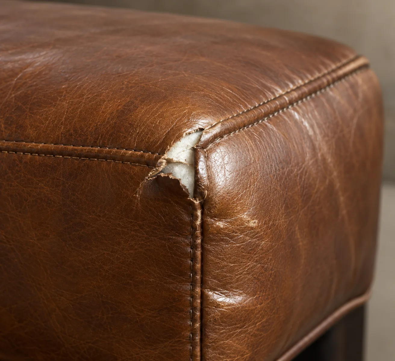 Brown bench corner with the seam stitching failed and the panel edges pulled apart