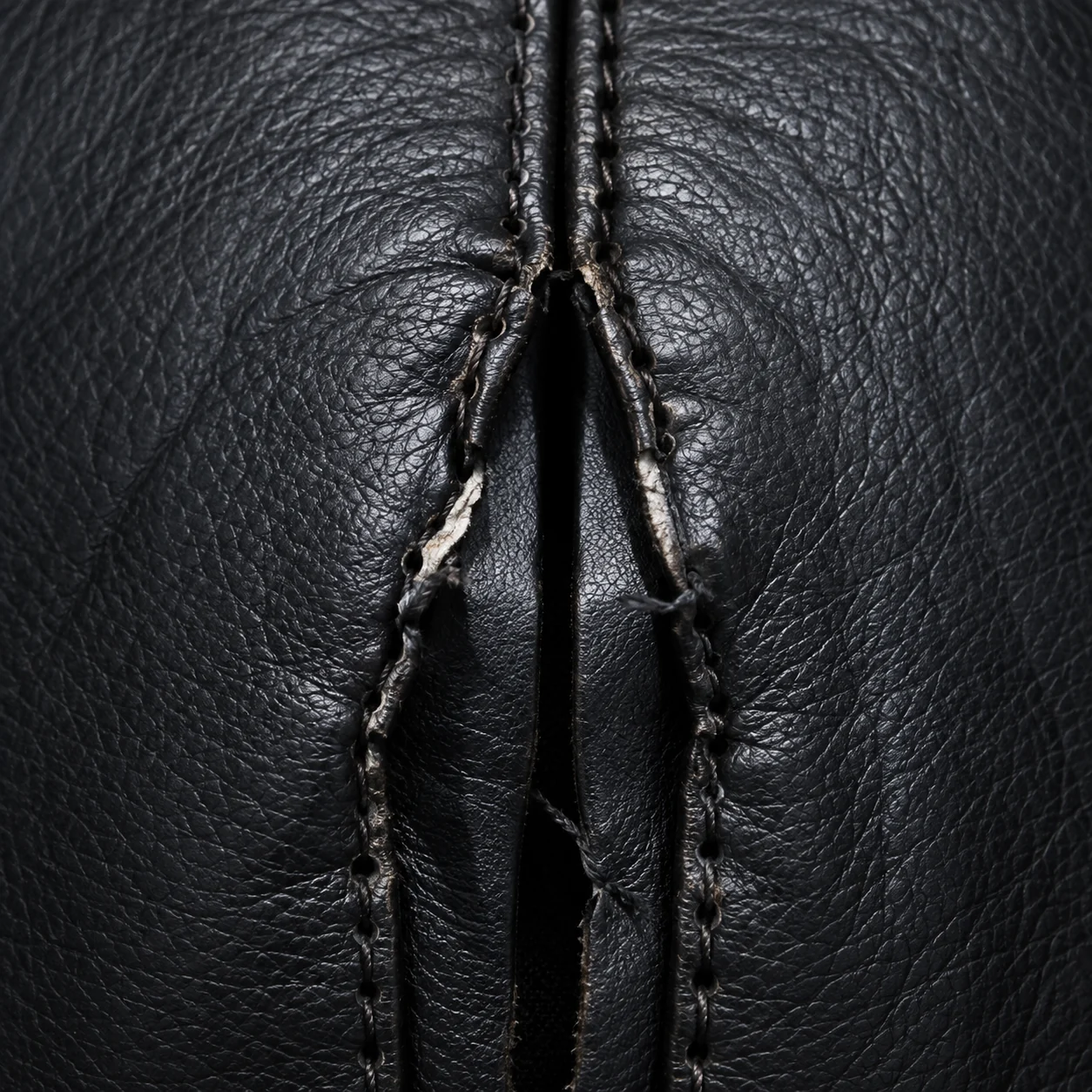 A burst seam on a black leather massage chair with the stitching broken open