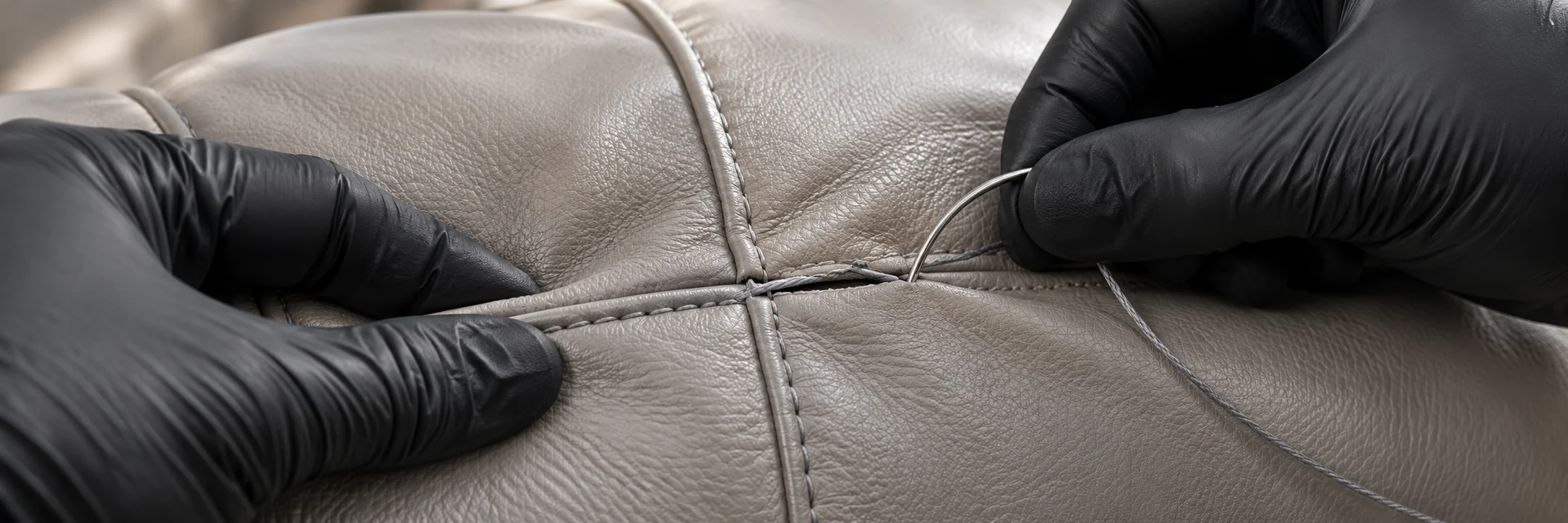 Gloved hands restitching a split seam in grey leather