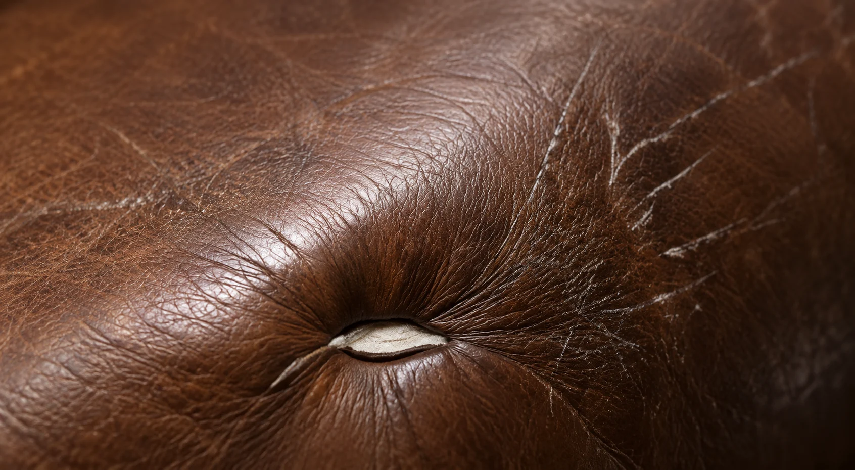 Cracks spreading outward from a single tufting button on a dark brown leather headboard