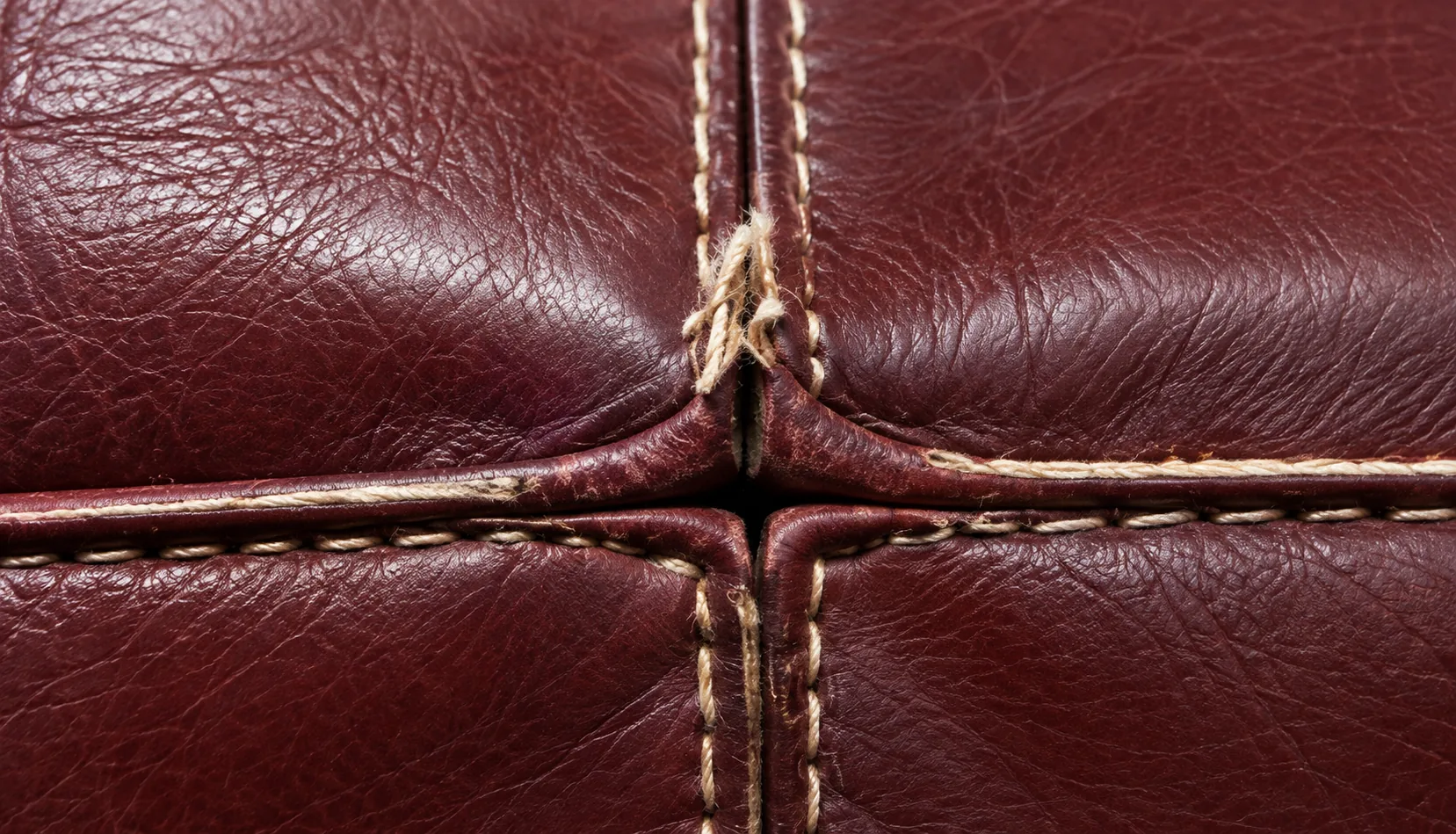 Open seam with pulled stitching on a burgundy leather seat