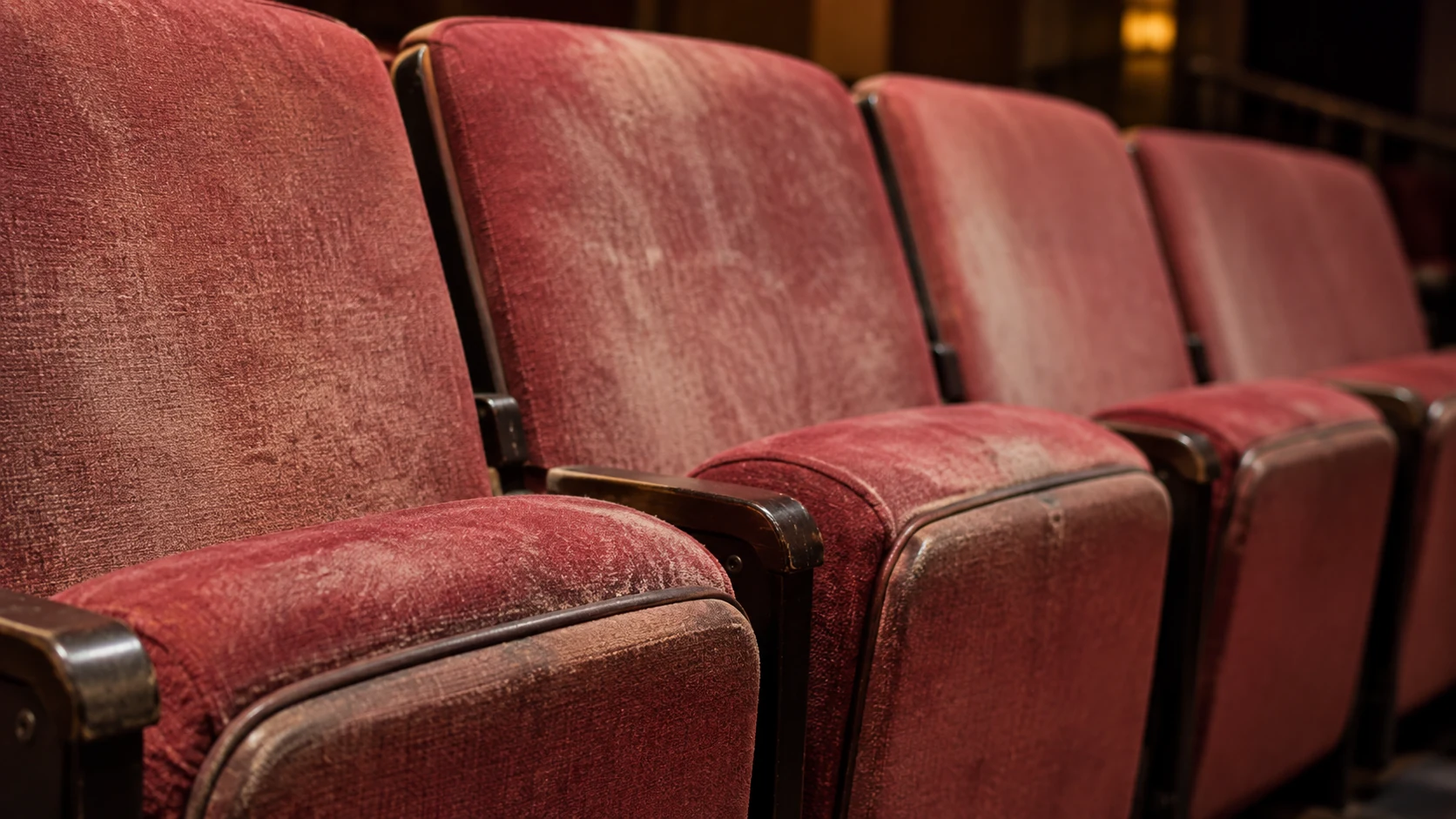 Faded red velvet theater seat covers in a row