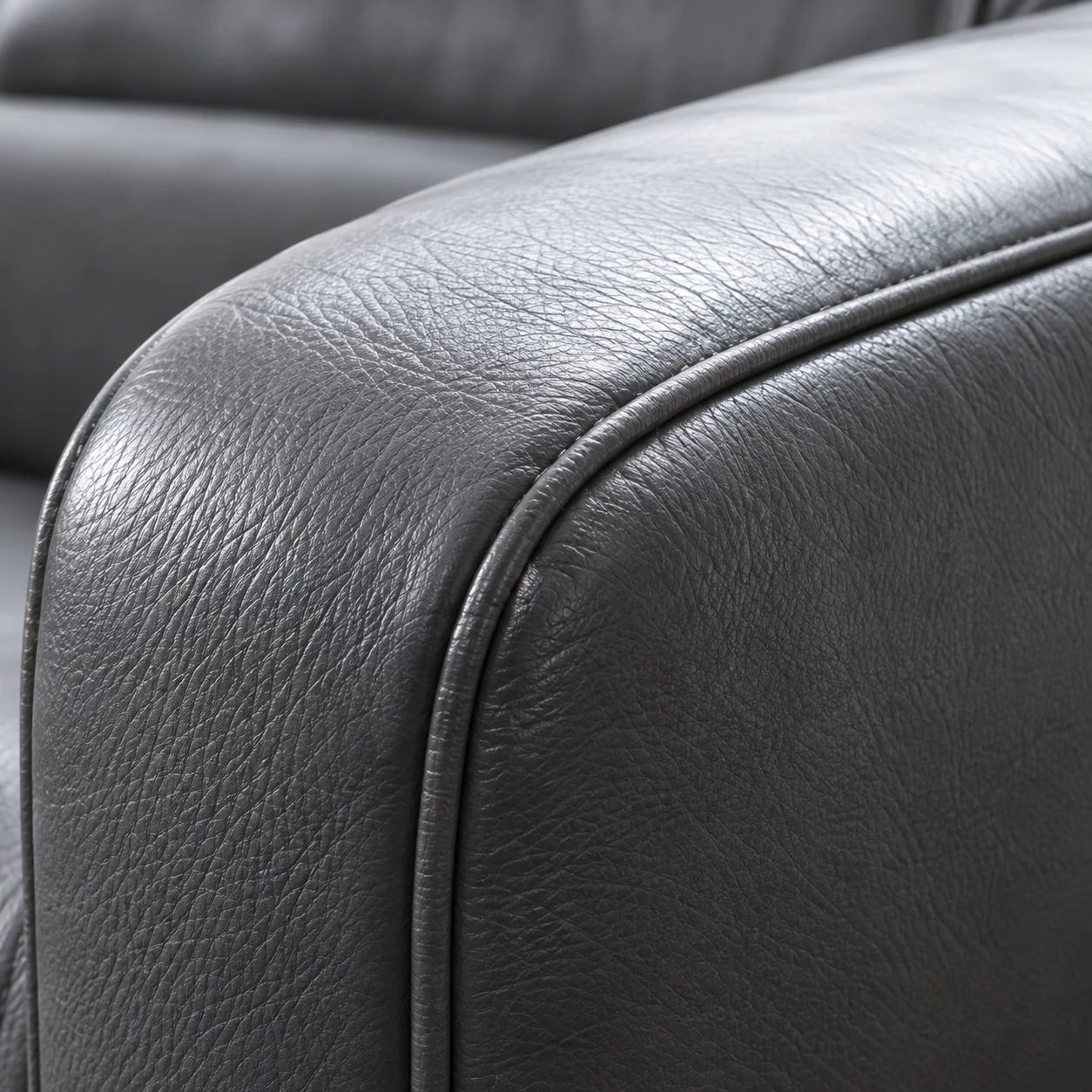 The rolled armrest of a gray leather sofa showing surface wear