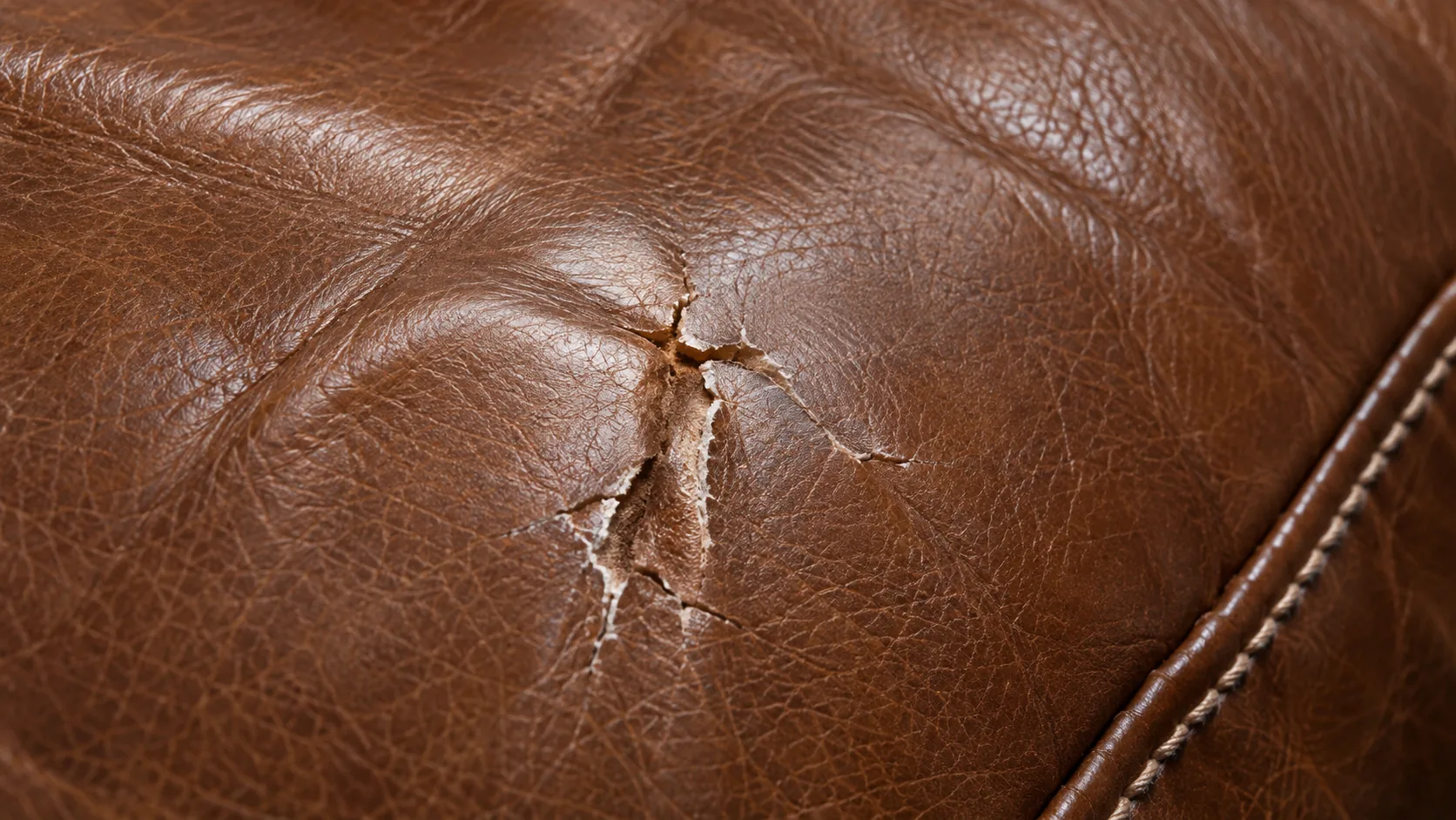 Close-up of a torn seam on a brown leather cushion
