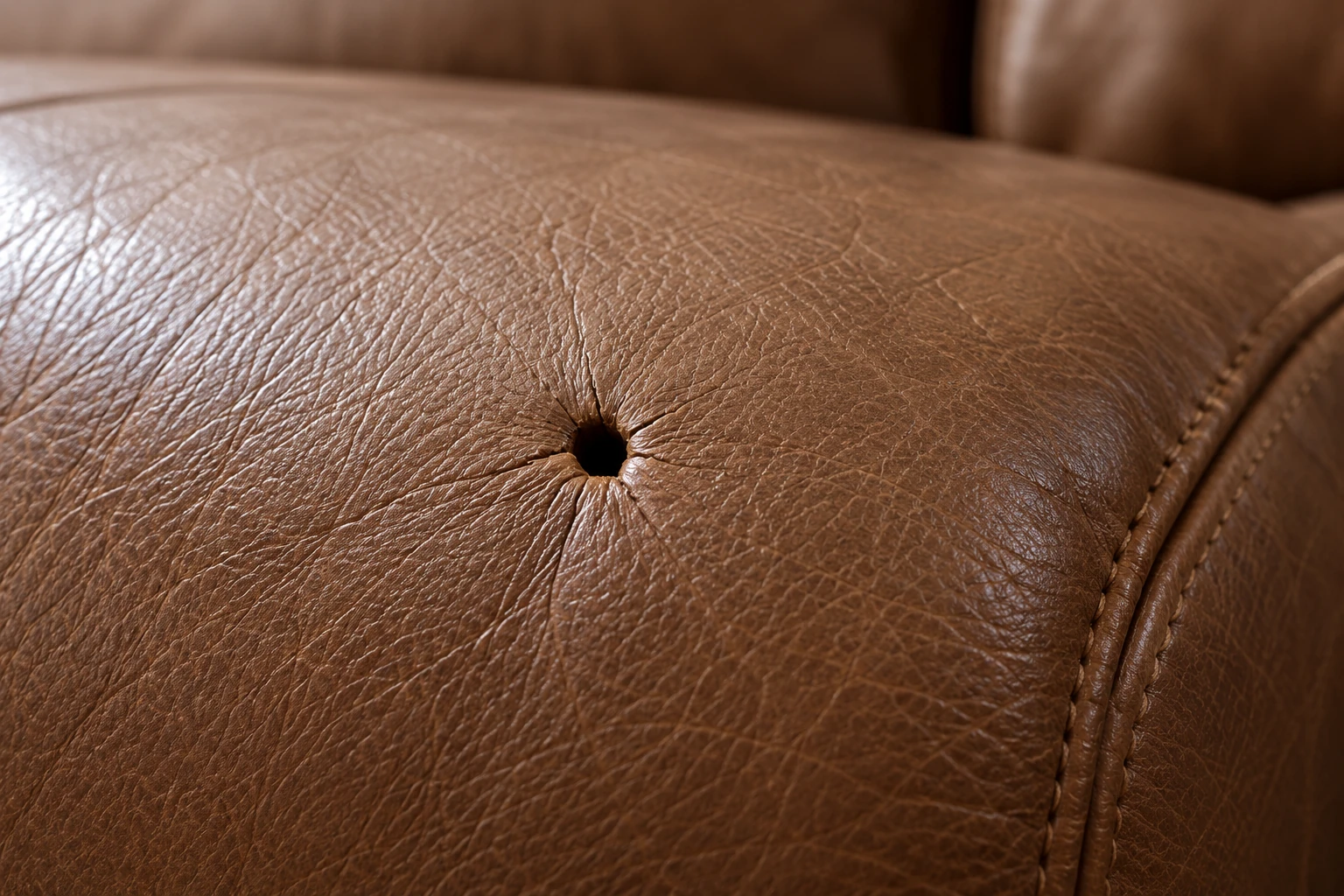 Small puncture in a tan leather seat before commercial leather furniture repair
