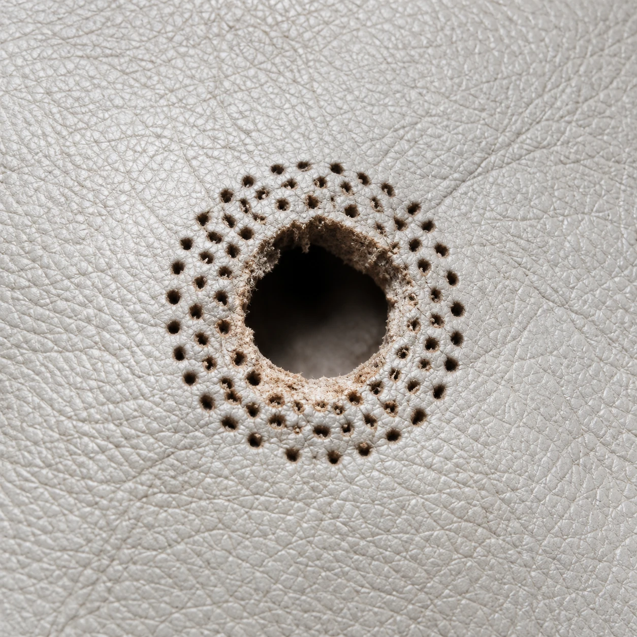 A round hole punched through pale leather upholstery