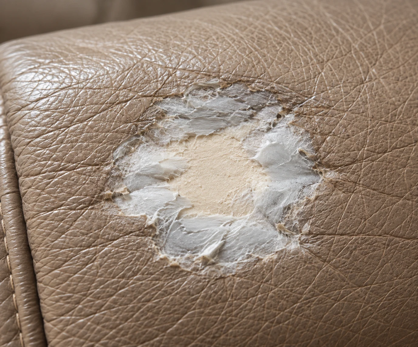 Large hole in taupe leather with foam showing
