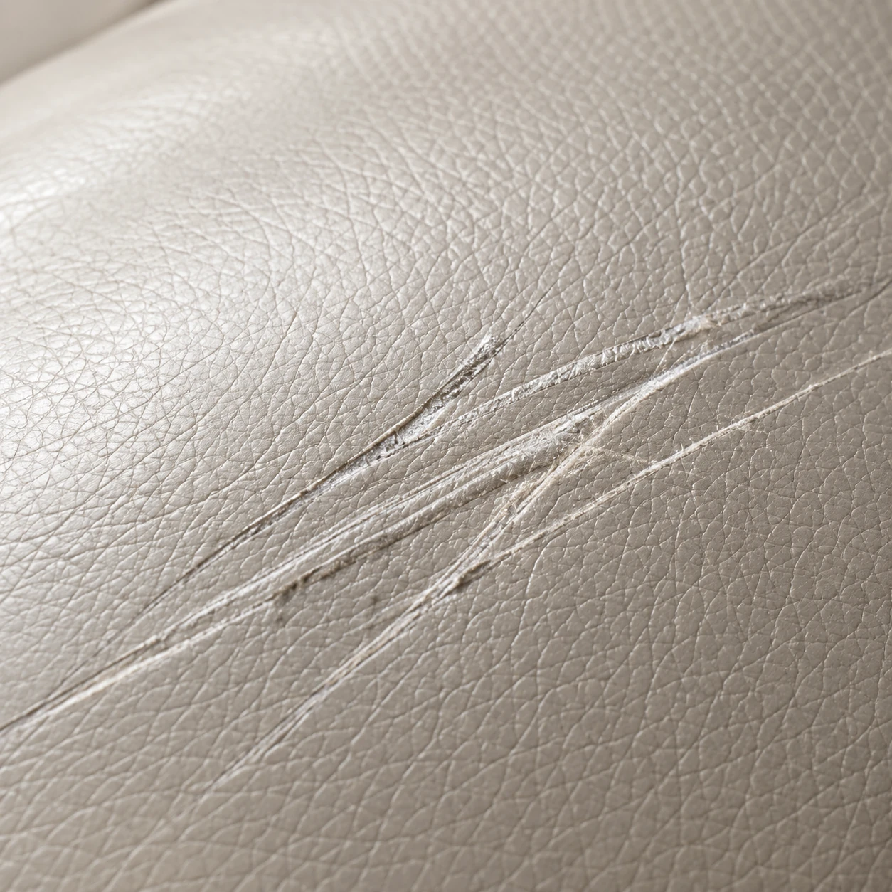 Fine surface scratches across a pale leather sofa cushion