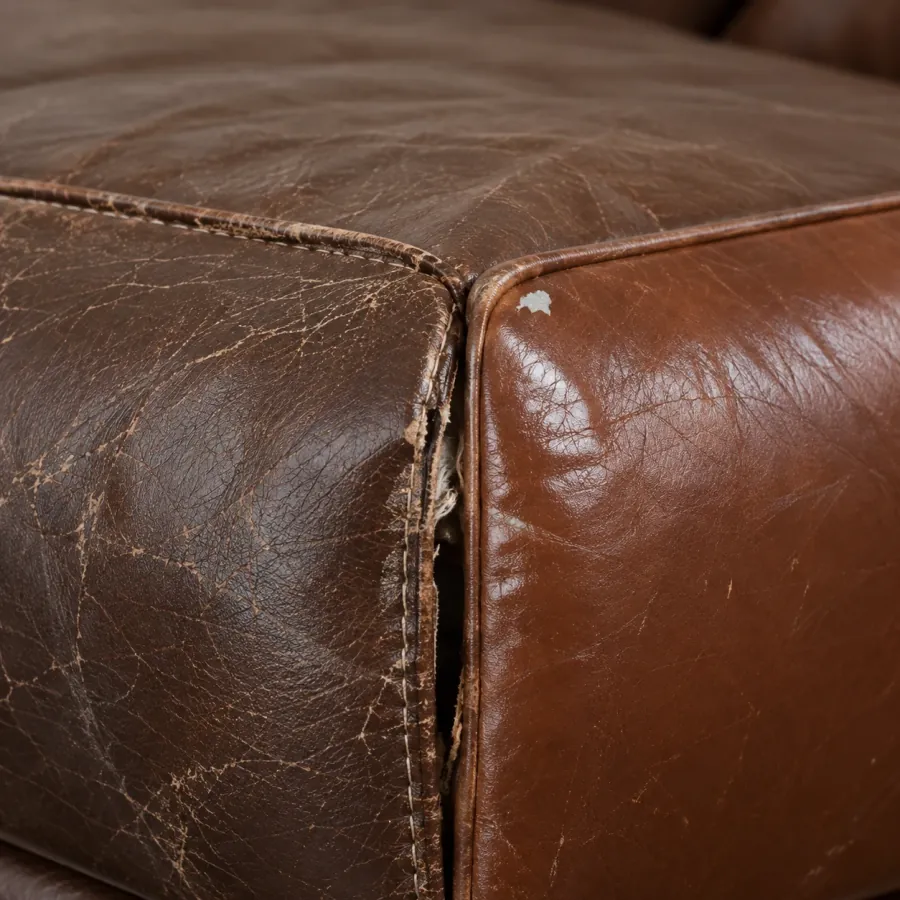 A brown leather corner where three seams meet, the leather stretched and distorted past the point of stitching