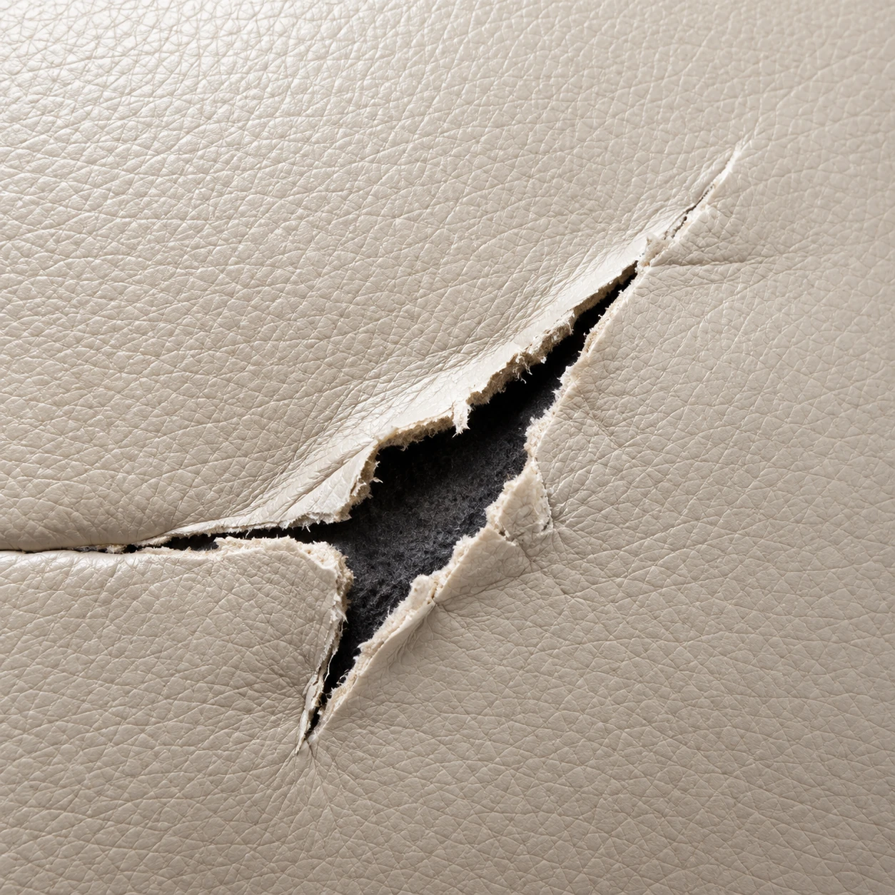 An open tear in a cream leather seat panel showing the layer beneath