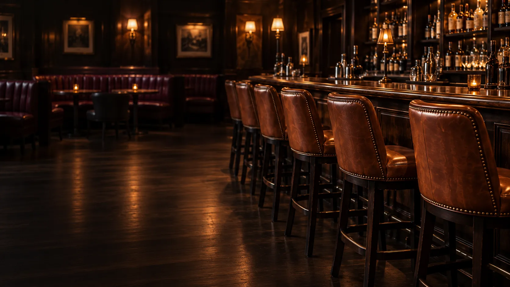 Lounge seating reupholstery NYC: a row of leather bar stools with nailhead trim along a lit back bar
