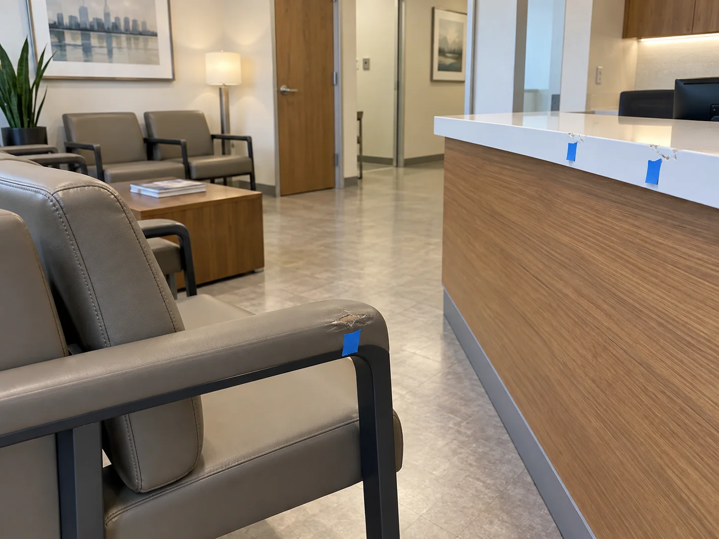 Blue tape markers beside damage on a waiting room chair arm and the check-in counter