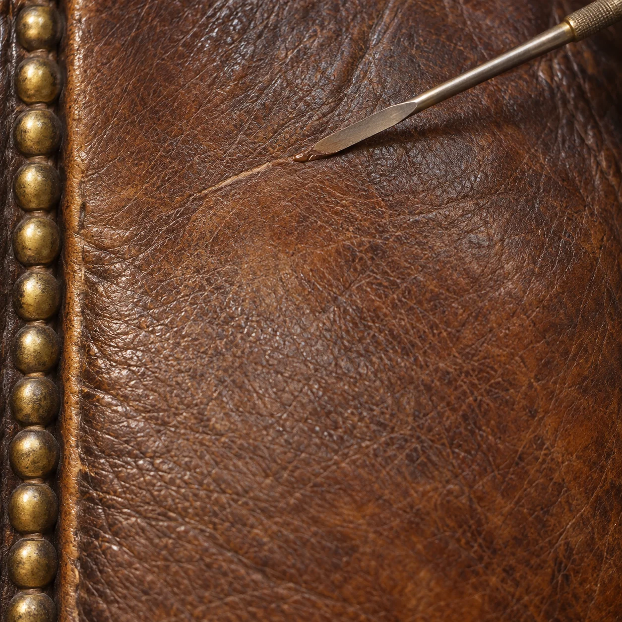 Brass nailhead trim beside a crack in the leather being probed