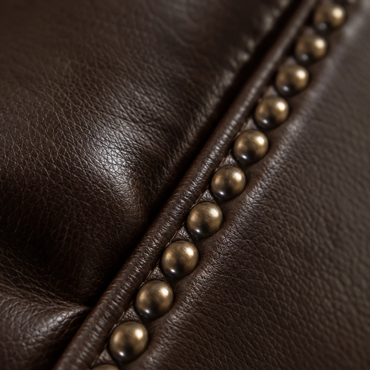 Antique brass nailhead trim running beside a welt on dark brown leather