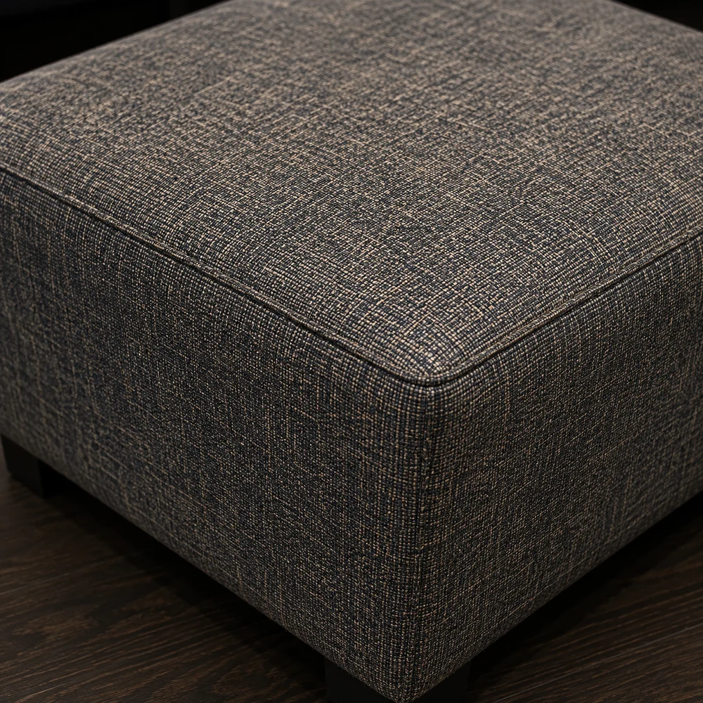 Corner of a gray woven fabric ottoman showing the texture of the weave