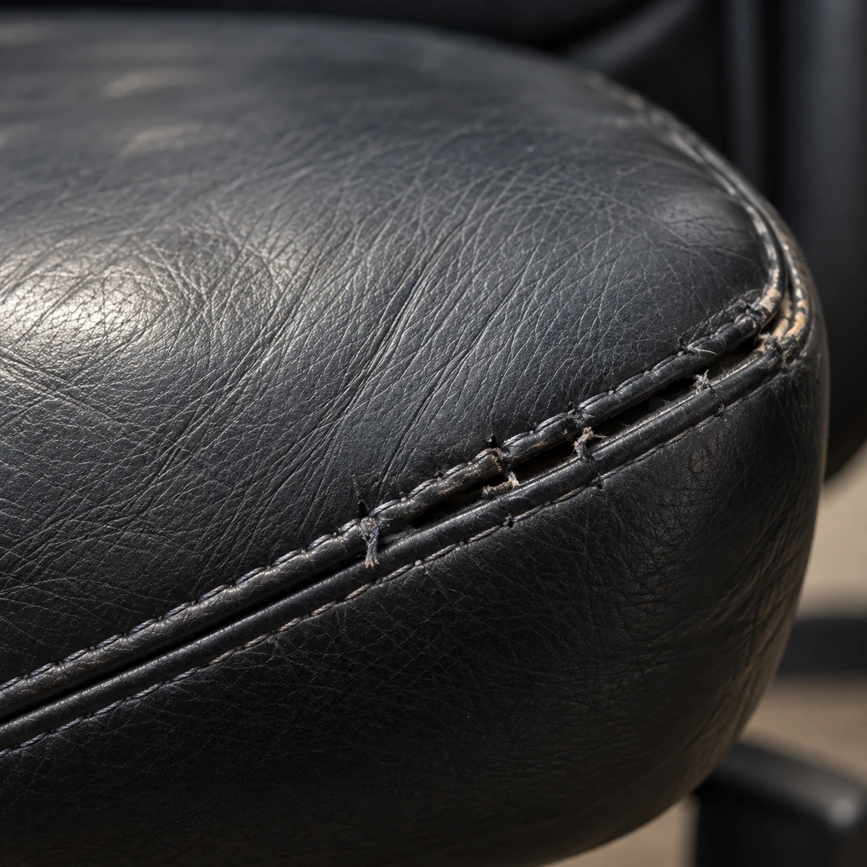 Worn front edge of an office chair seat with creasing along the stitch line