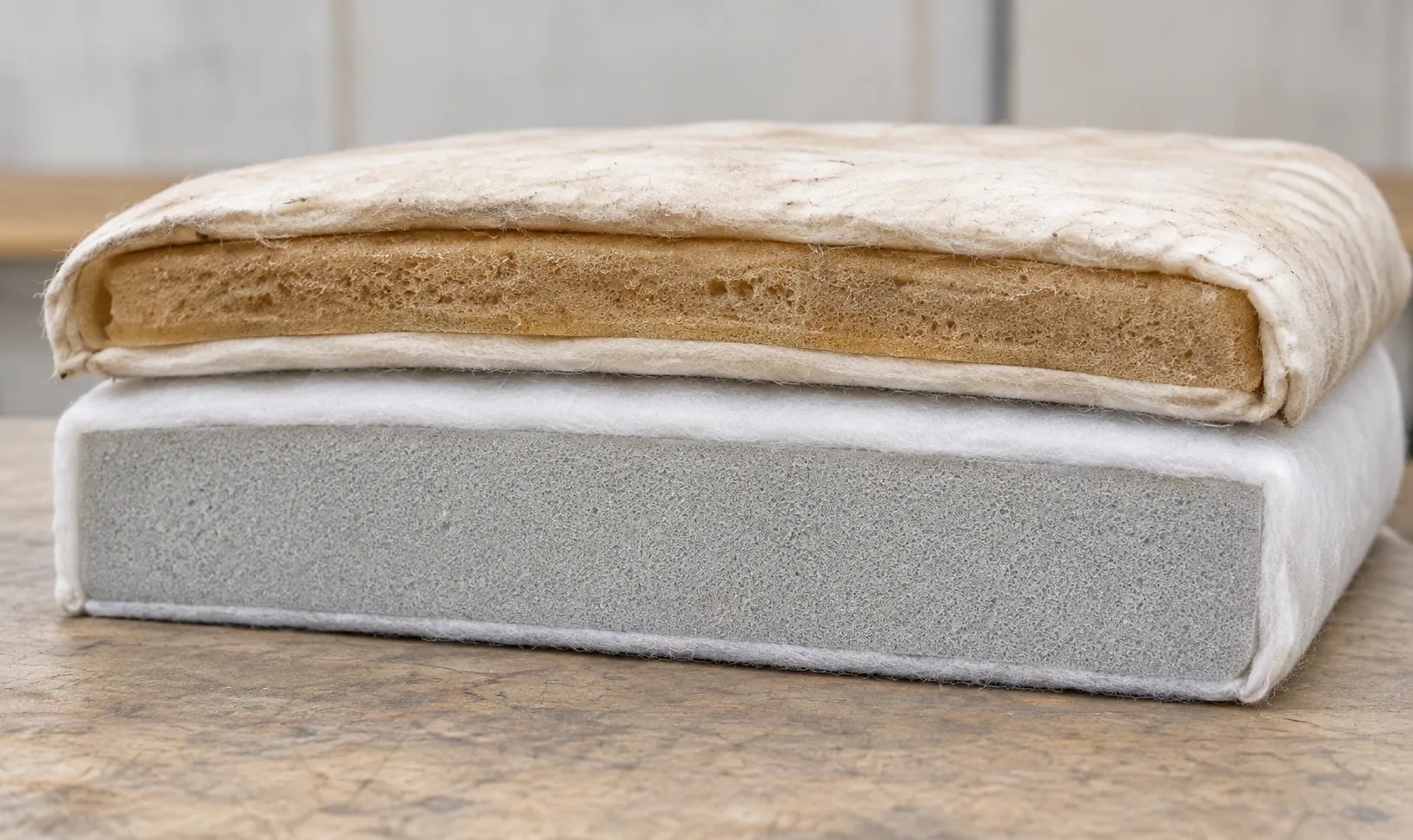 Yellowed foam and its batting wrap lying on top of a new grey foam cushion core