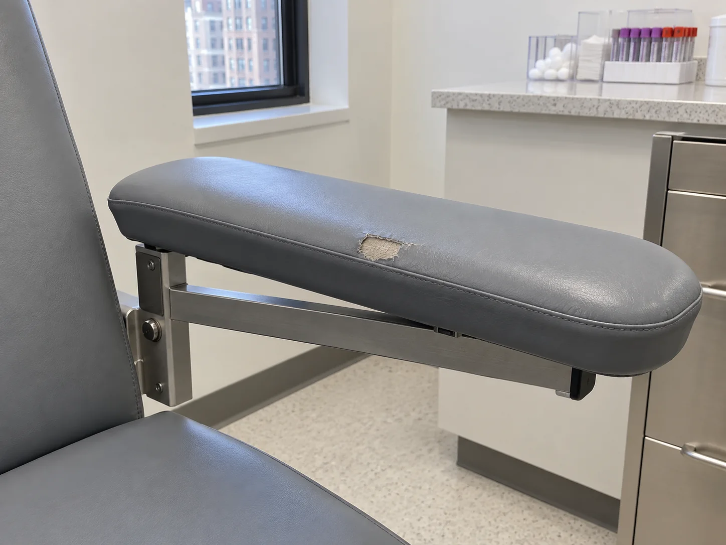 A phlebotomy chair armrest pad worn through to the fabric backing at the elbow area