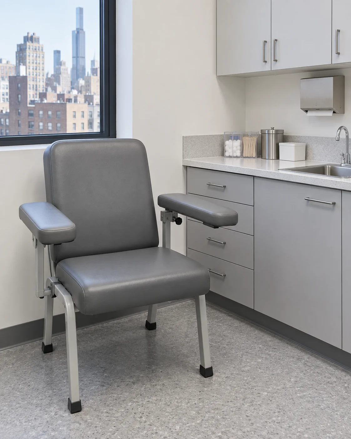 A grey vinyl phlebotomy draw chair with a flip-up armrest beside a lab counter