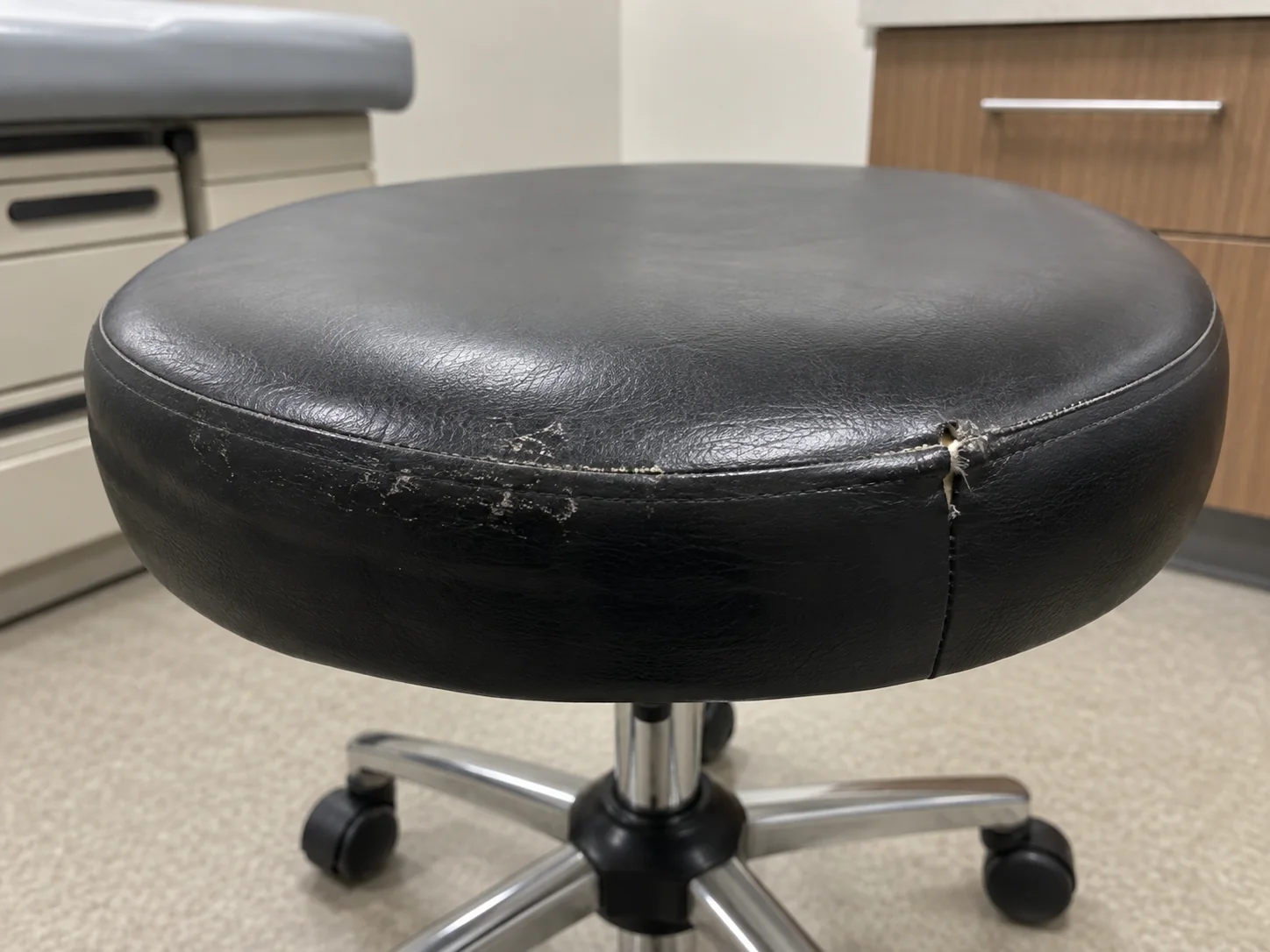 A physician stool with a scuffed seat edge and an opened side seam