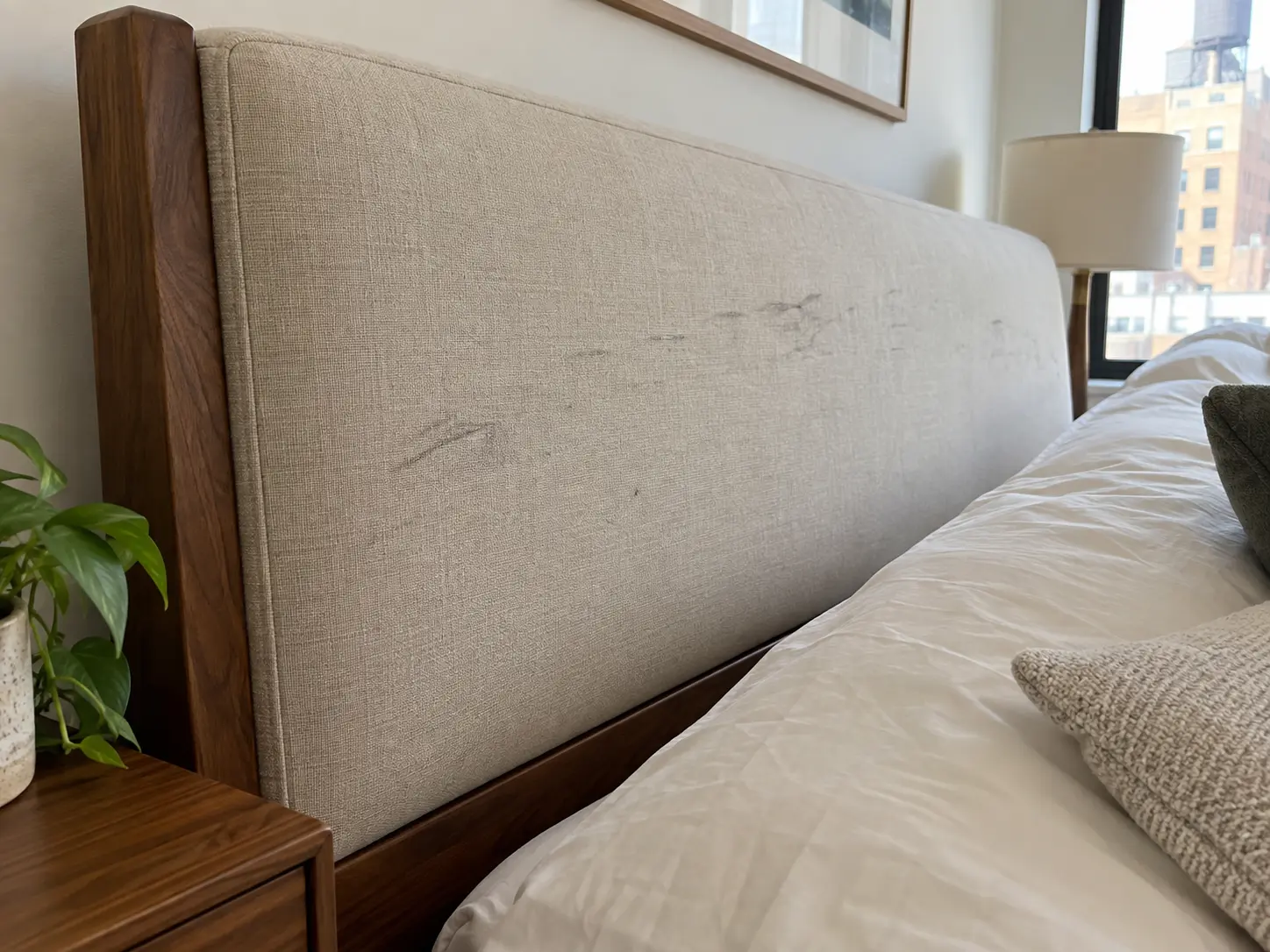 A scuffed upholstered headboard in a rental bedroom