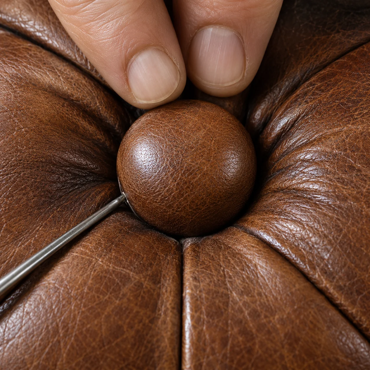 Antique leather sofa repair: a deep button being re-tied with a long needle