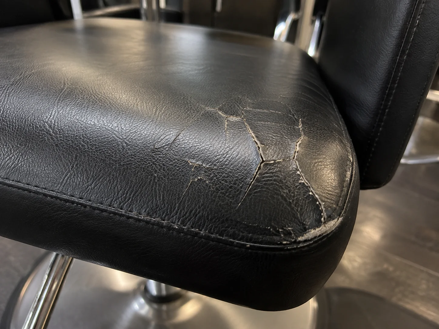 Cracked black vinyl at the front edge of a salon chair seat